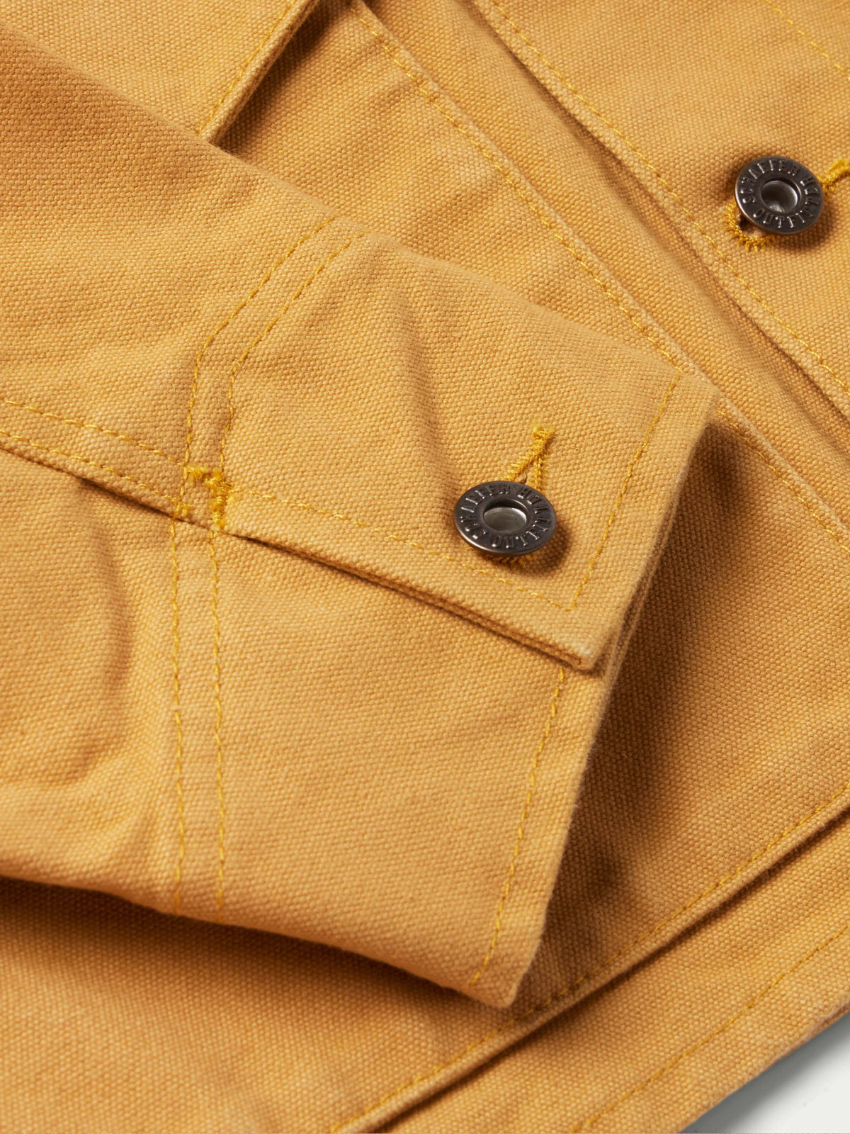 Suntan brush jacket cuff close-up with button and reinforced stitching.