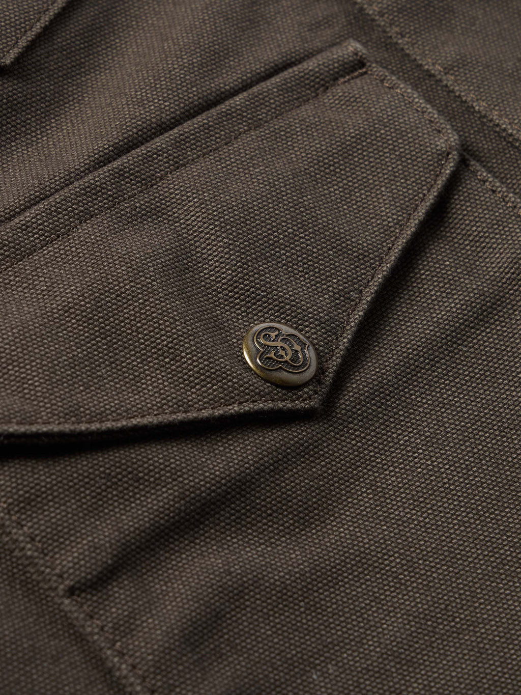Brown canvas jacket front flap with stitched tab and metal logo button