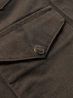 Brown canvas jacket front flap with stitched tab and metal logo button