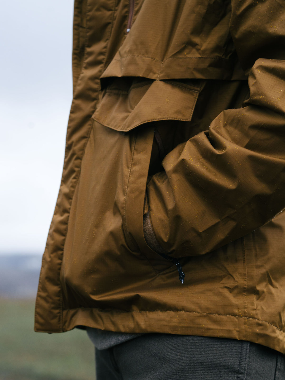 Brown rain jacket front with zip, pocket flap, and hood drawcord