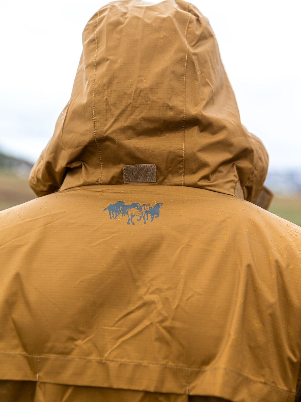 Brown rain jacket with attached hood, back logo, and adjustable drawcord