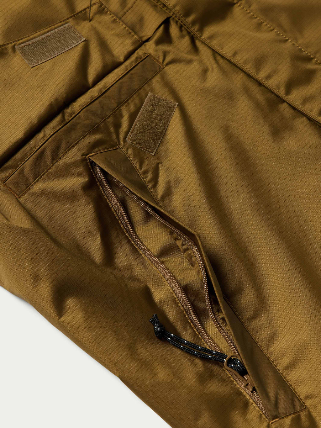Brown rain jacket pocket and zipper detail with fabric tab