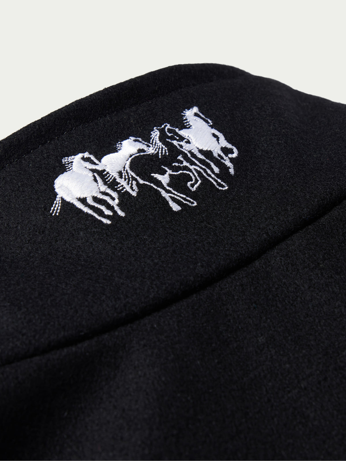 Black wool vest close-up with white and blue embroidered horse logo on shoulder