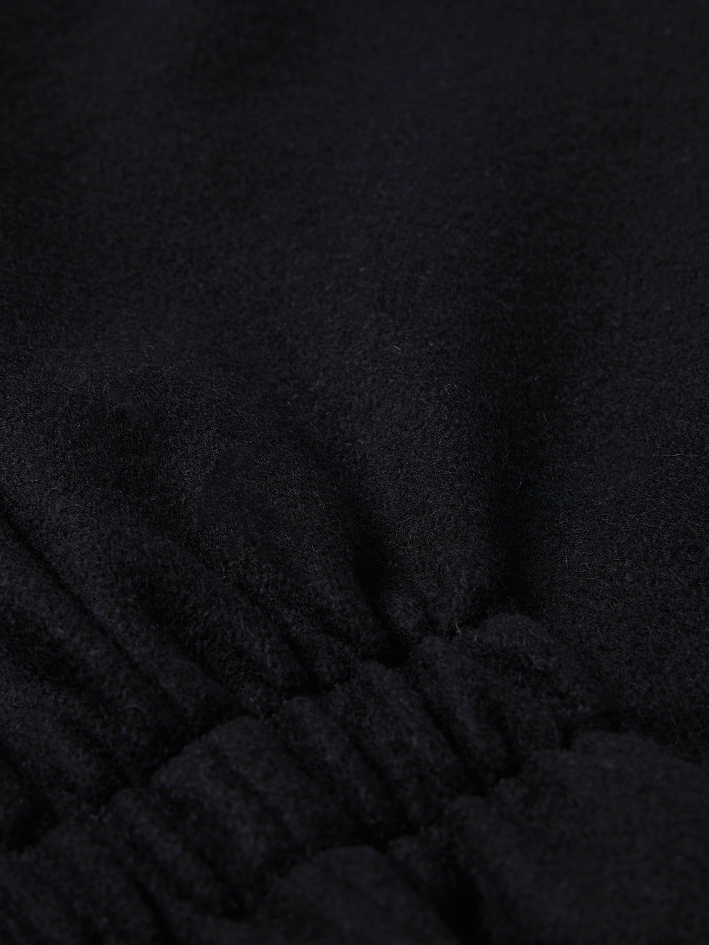 Black wool vest fabric close-up with stitched seam at the lower front