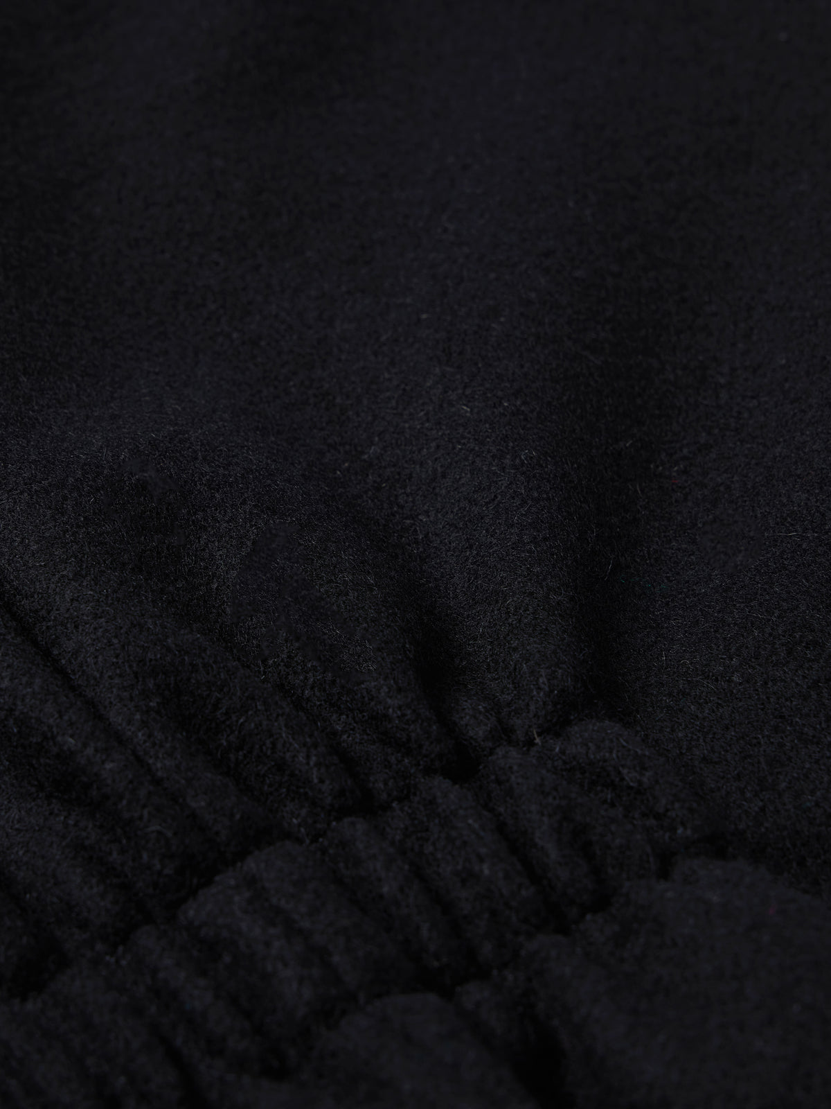 Black wool vest fabric close-up with stitched seam at the lower front