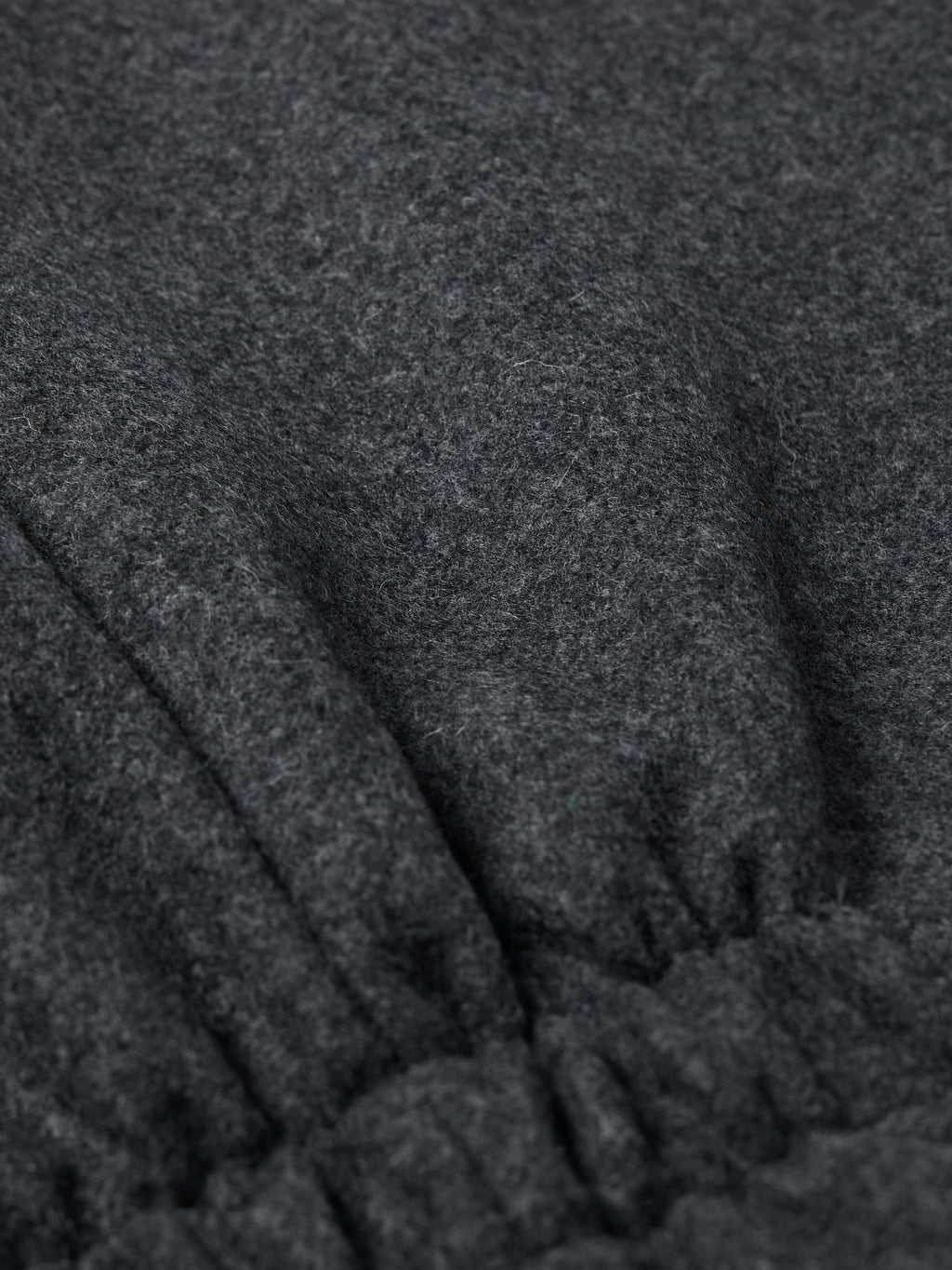 Charcoal wool vest close-up with gathered hem seam and textured fabric
