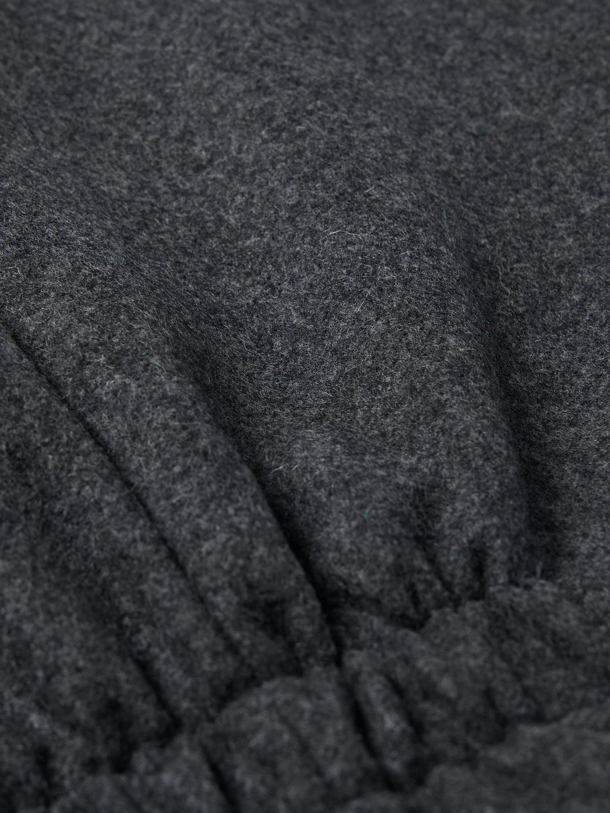 Charcoal wool vest close-up with gathered hem seam and textured fabric