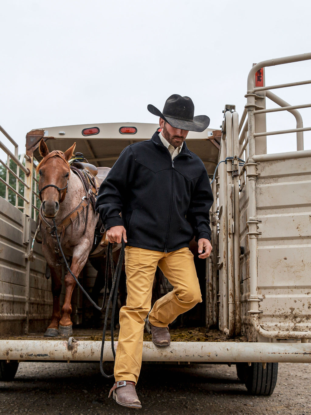 Black wool arena jacket worn by rider near trailer, stand collar and zipper