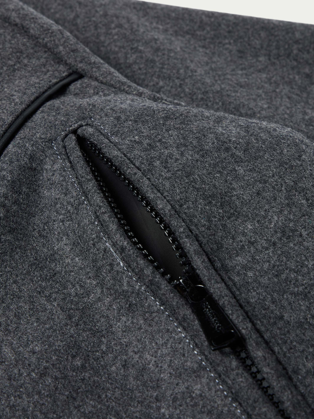 Charcoal wool coat detail: black zip pocket trim and stitched seam