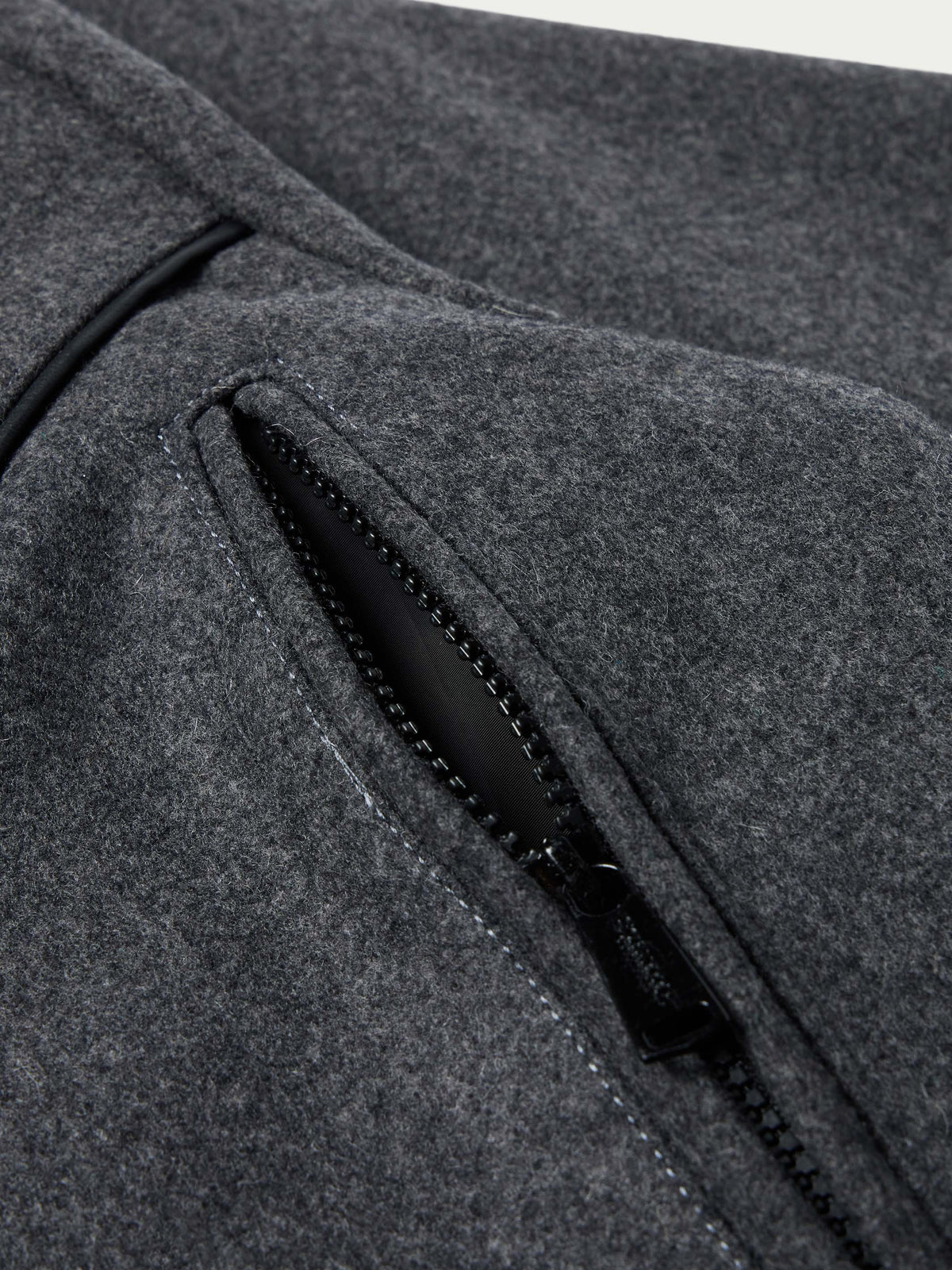 Charcoal wool coat detail: black zip pocket trim and stitched seam