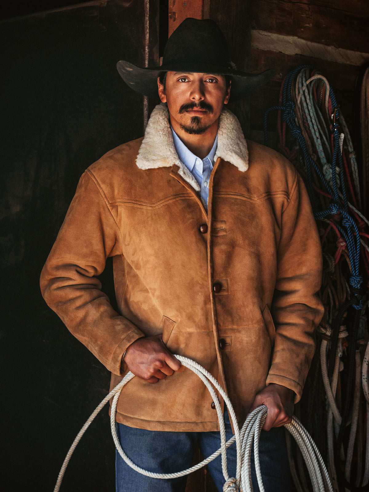 Man wearing a buckskin shearling coat with cream collar, button front, and side pockets