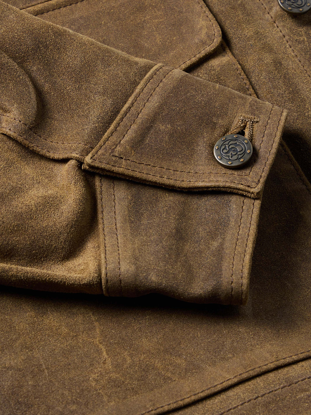 Tan leather jacket cuff and pocket flap with snap closure, stitched detail close-up.