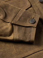 Tan leather jacket cuff and pocket flap with snap closure, stitched detail close-up.