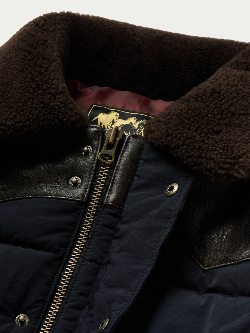 Navy puffer jacket collar detail with brown leather trim and gold-tone zipper