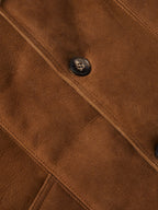 Brown suede shearling coat detail: diagonal seam and round black button.