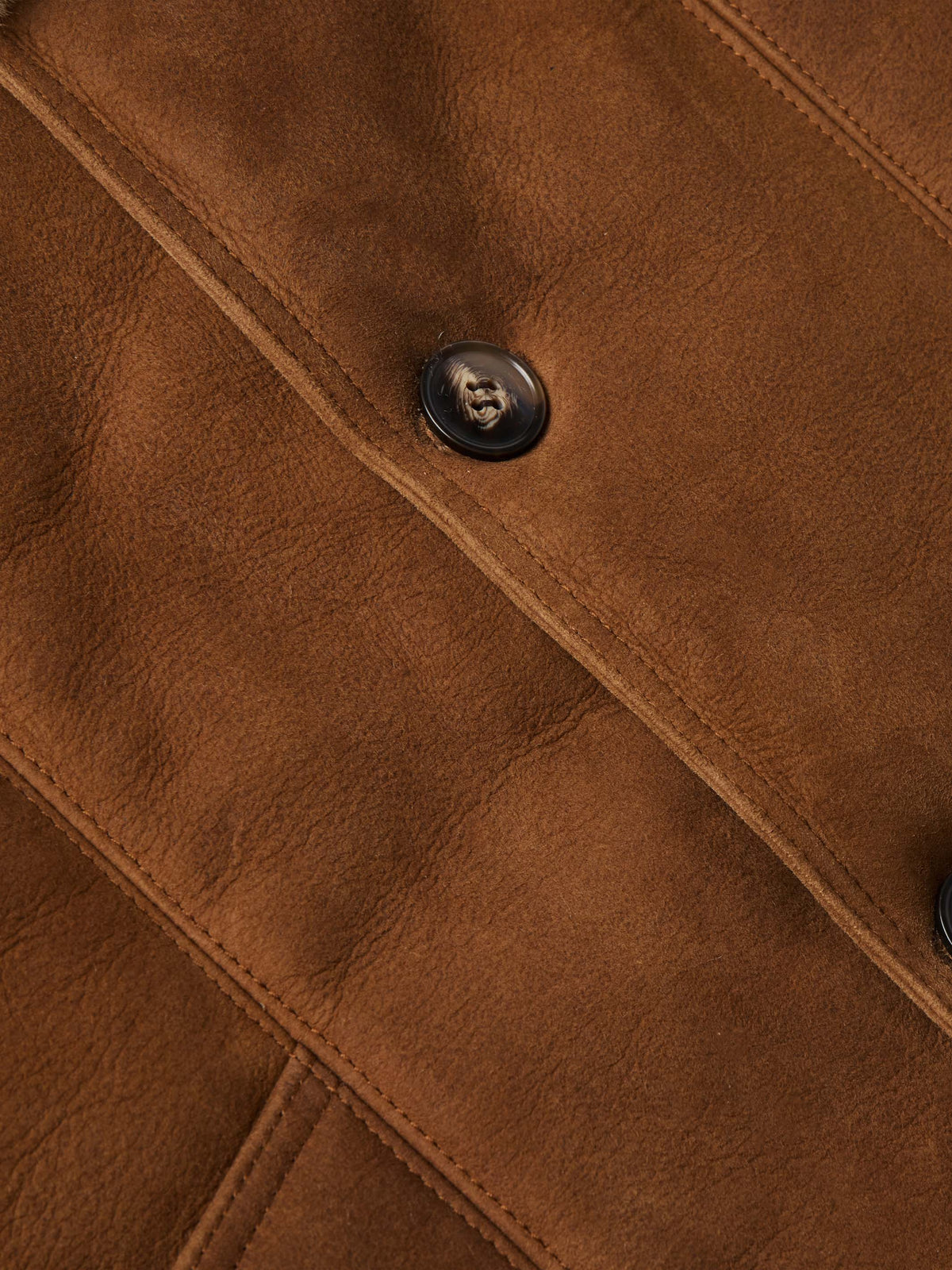 Brown suede shearling coat detail: diagonal seam and round black button.