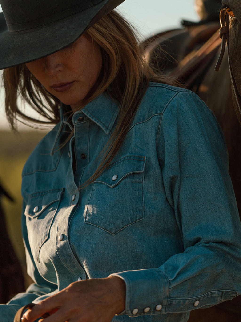 Woman wearing light wash denim western shirt with two chest pockets and pearl snaps
