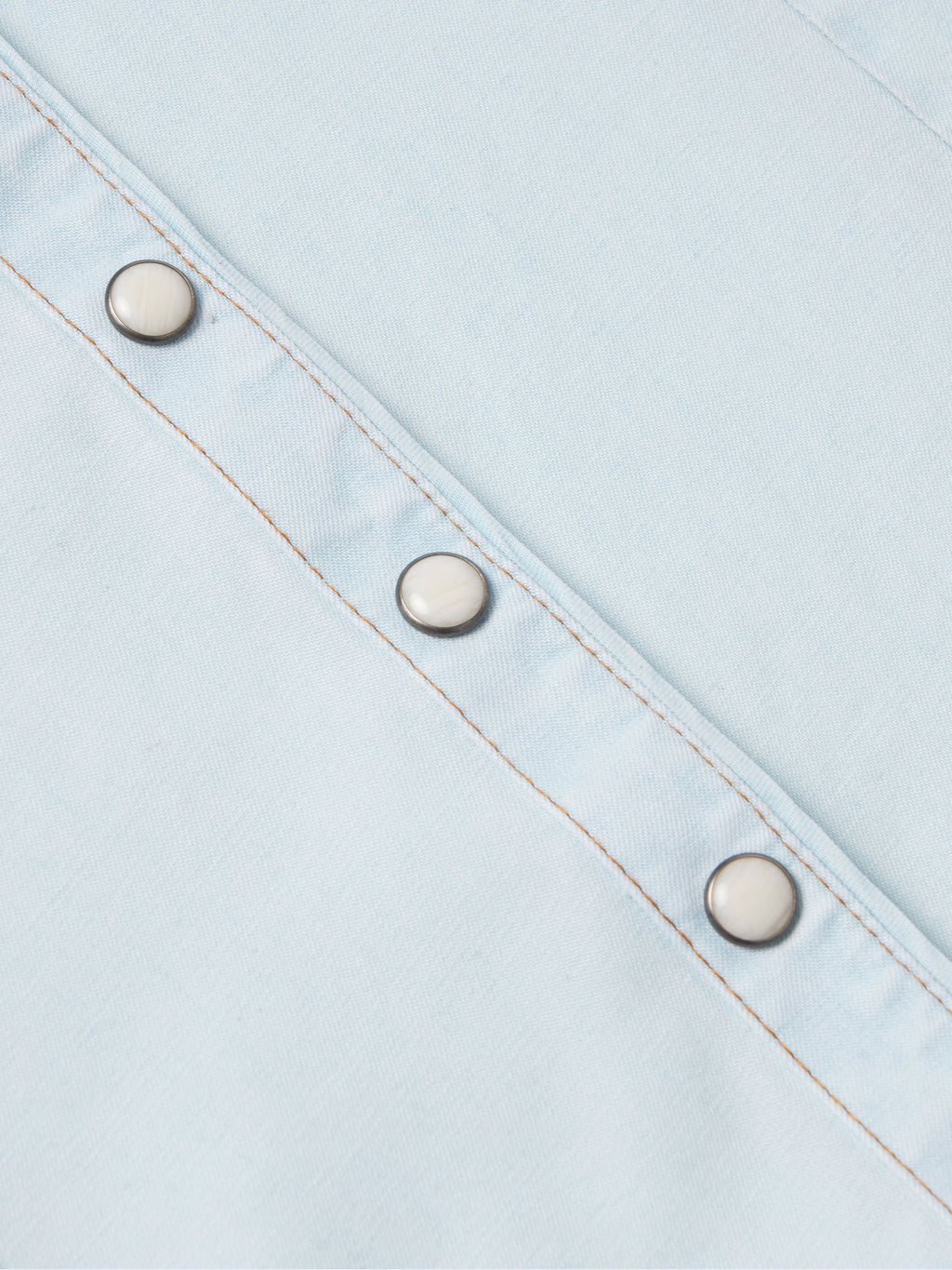 Light wash denim snap shirt sleeve placket with three metal snaps and orange stitching