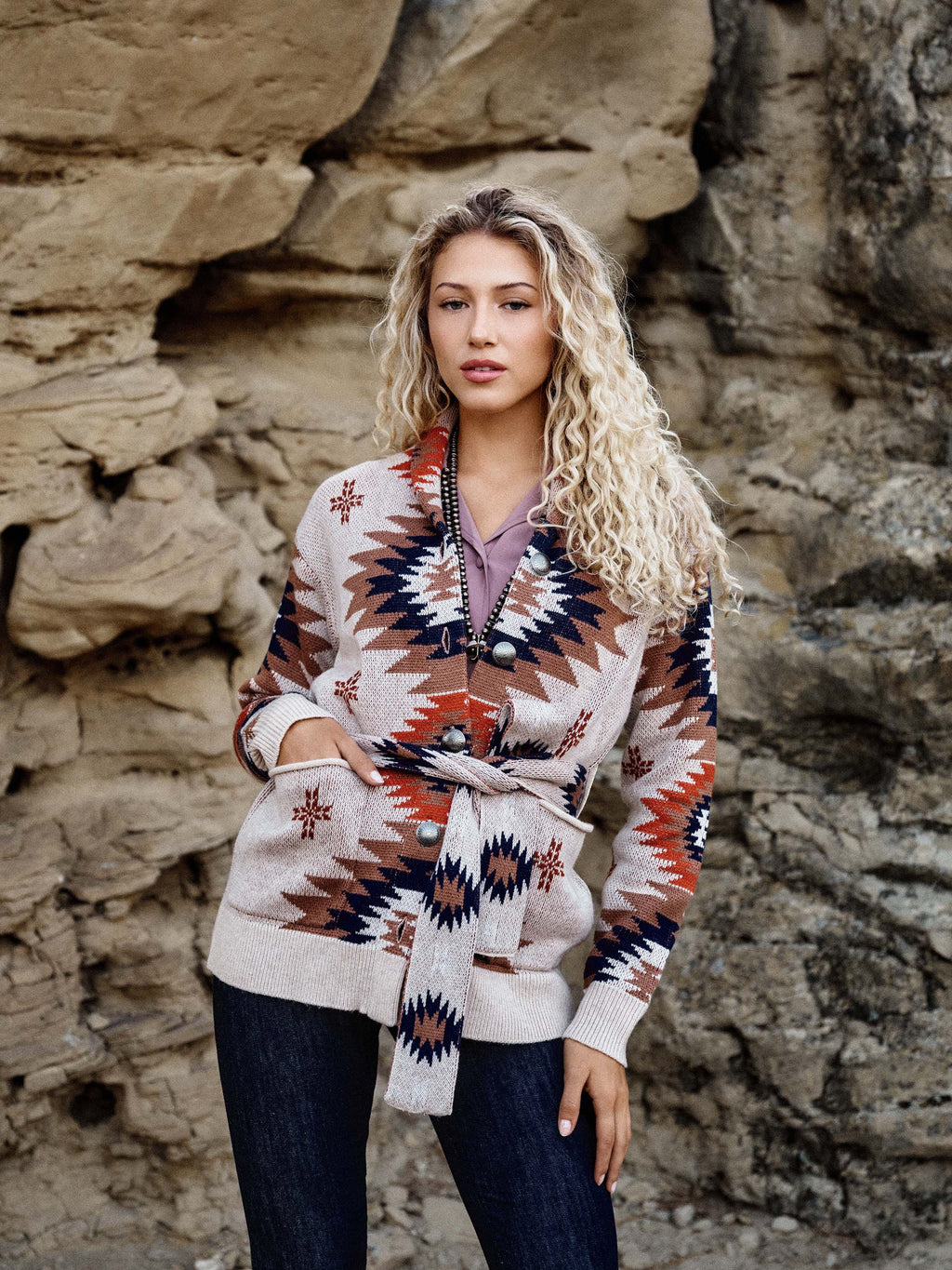 Women's belted sweater worn, cream knit with geometric orange and navy pattern.