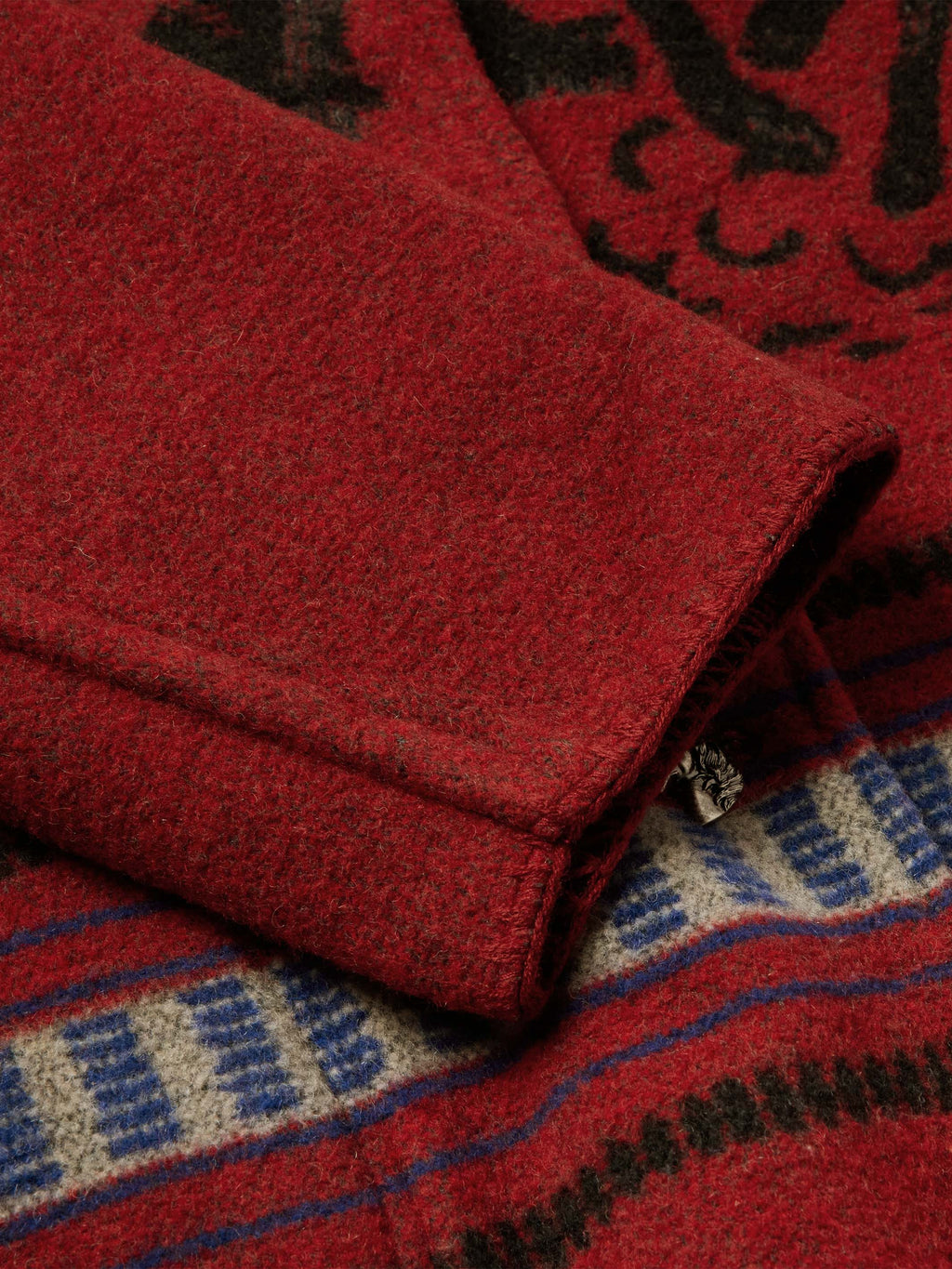 Crimson blanket-style coat sleeve cuff with patterned lining and metal button