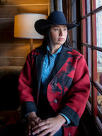 Crimson blanket-style coat with dark trim, blue shirt, and wide-brim hat