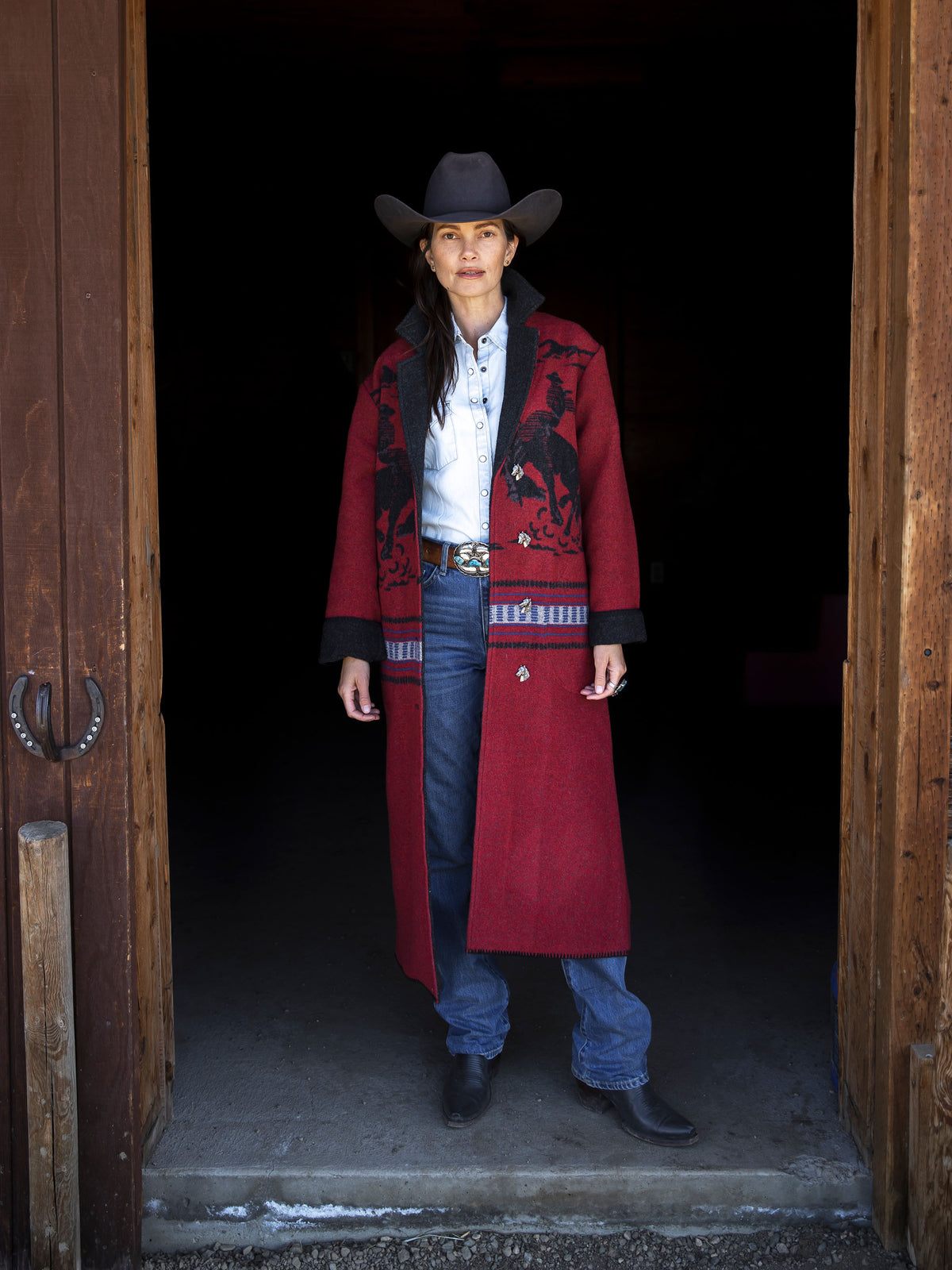 Woman wearing crimson blanket coat over jeans with dark hat and blue shirt