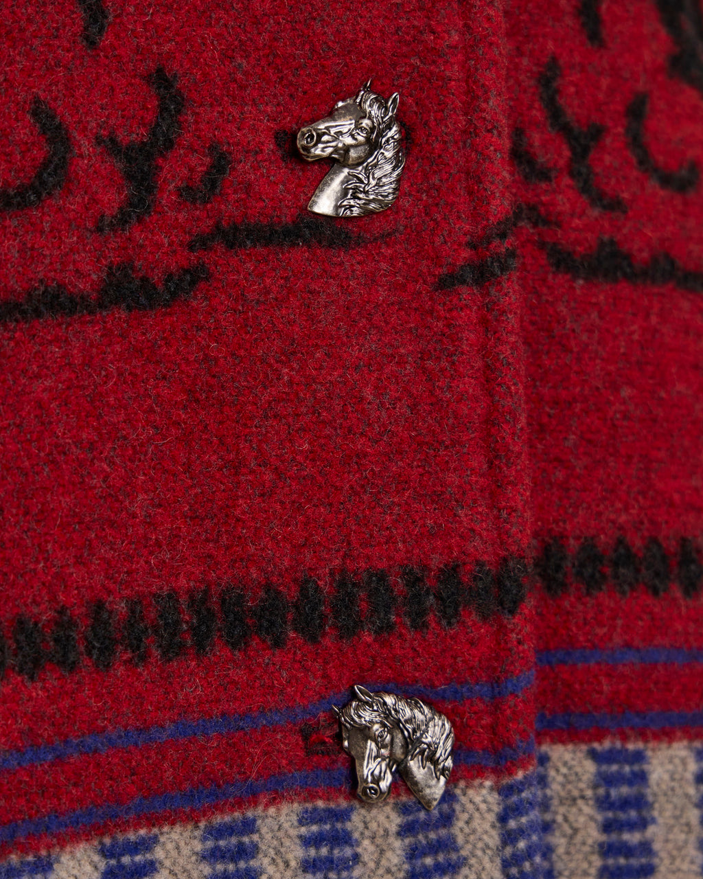 Crimson red blanket coat fabric close-up with horse-head patch and blue trim.
