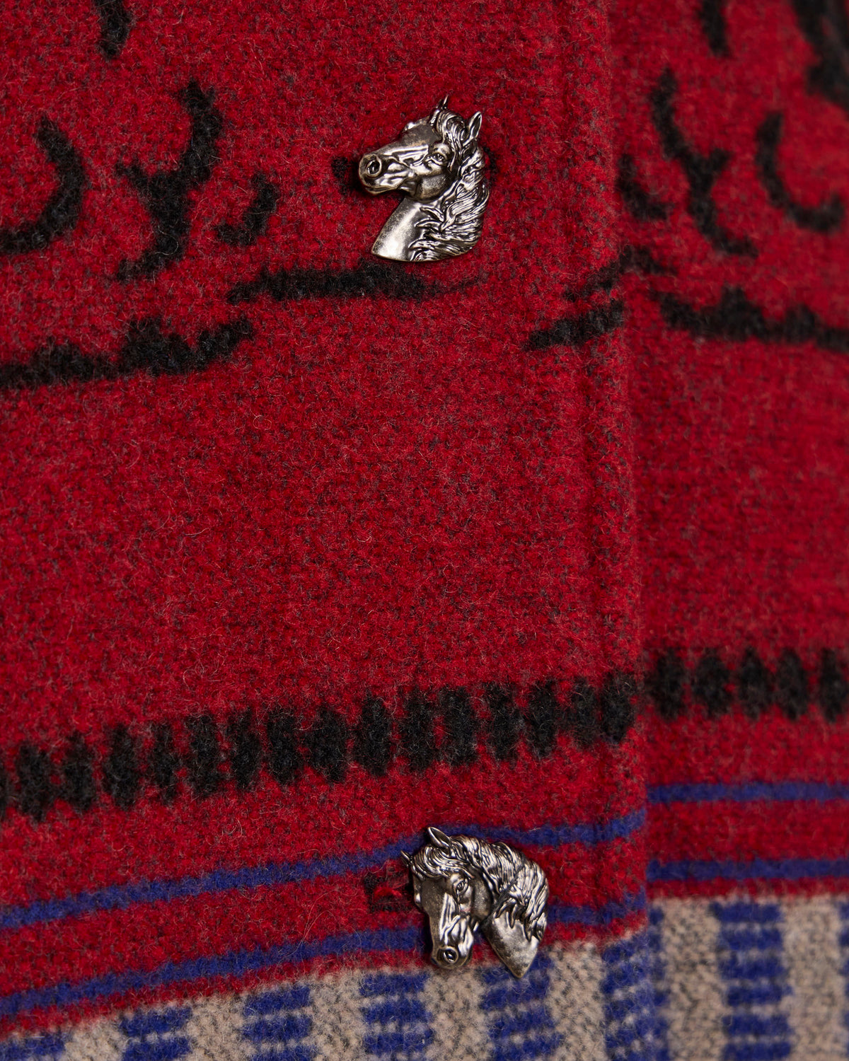 Crimson red blanket coat fabric close-up with horse-head patch and blue trim.