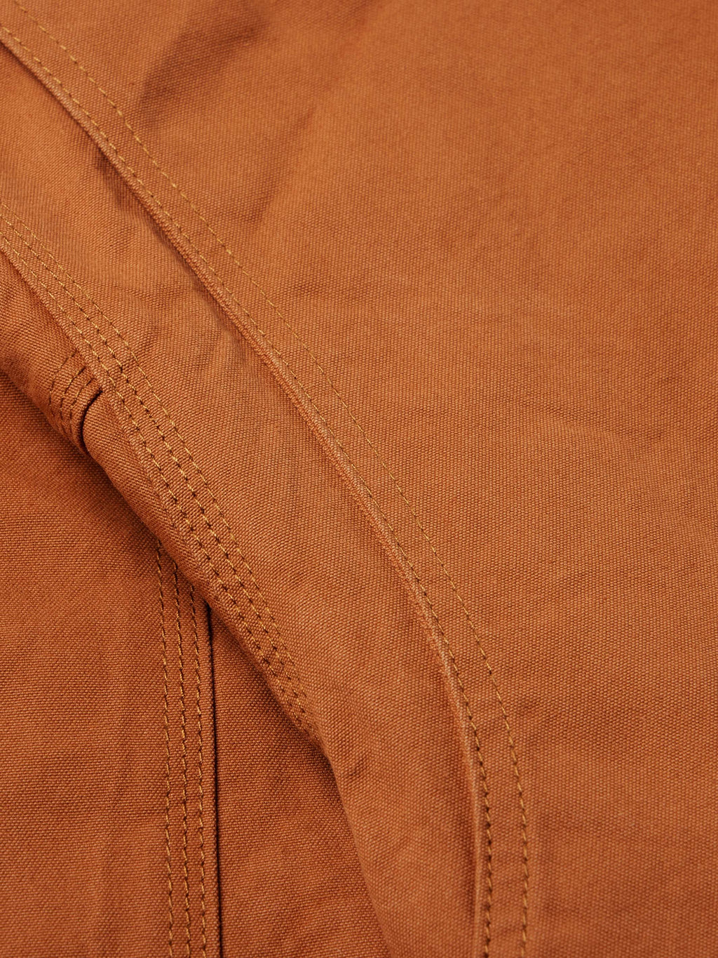 Close-up of rust-orange jacket seam detail with double stitching and reinforced panels