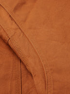 Close-up of rust-orange jacket seam detail with double stitching and reinforced panels