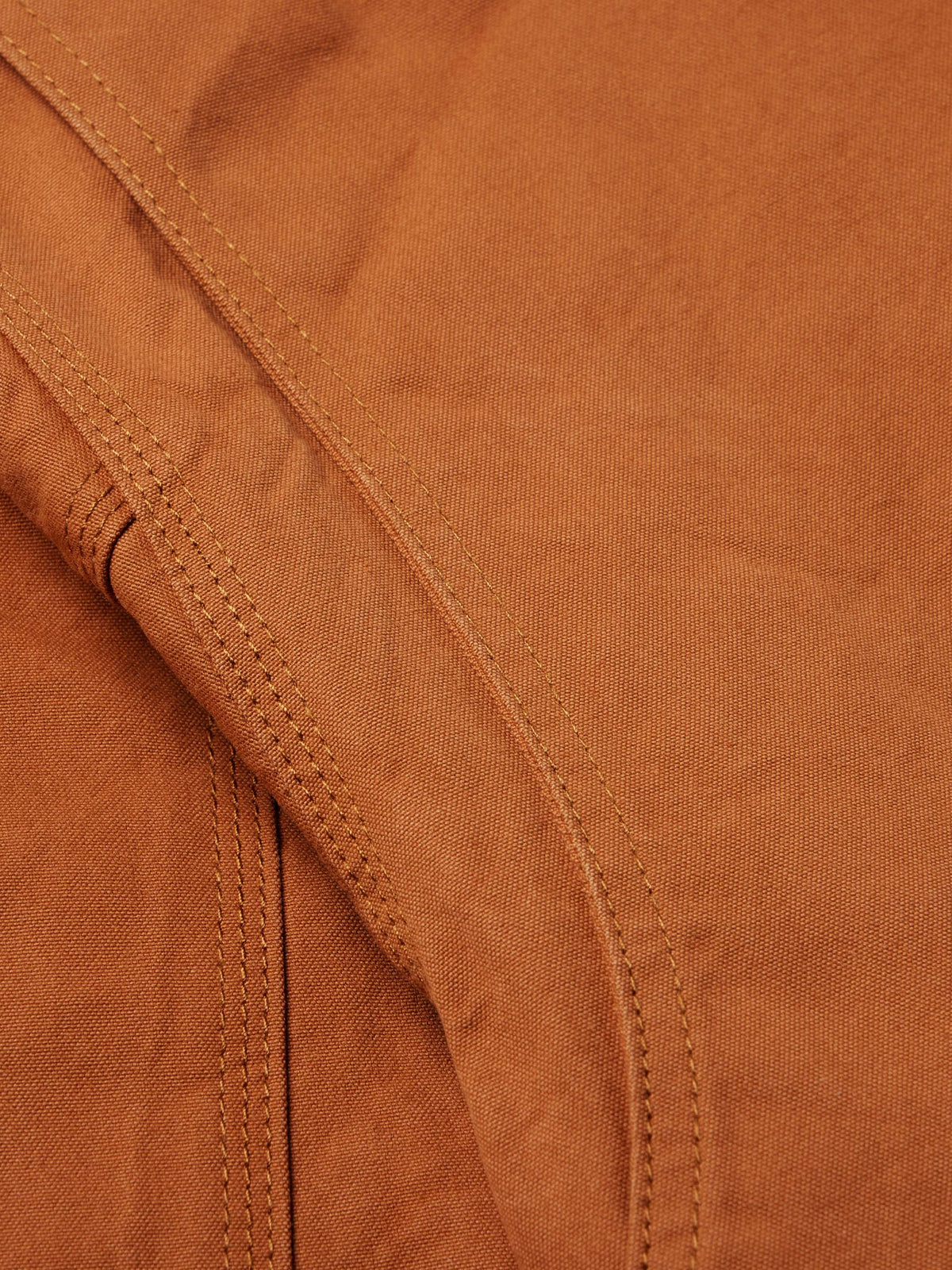 Close-up of rust-orange jacket seam detail with double stitching and reinforced panels