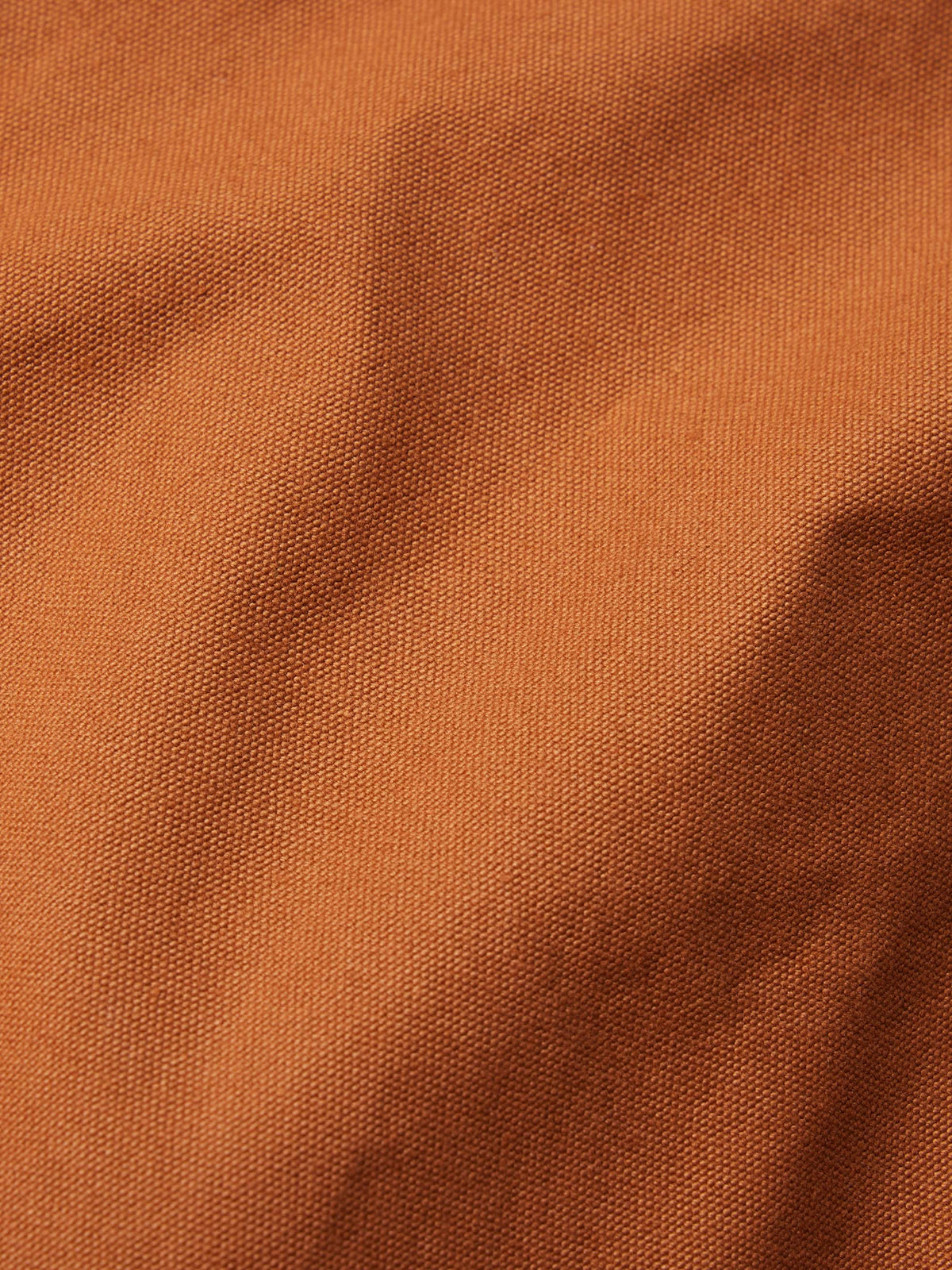 Close-up fabric texture of rust-orange cotton with visible woven grain