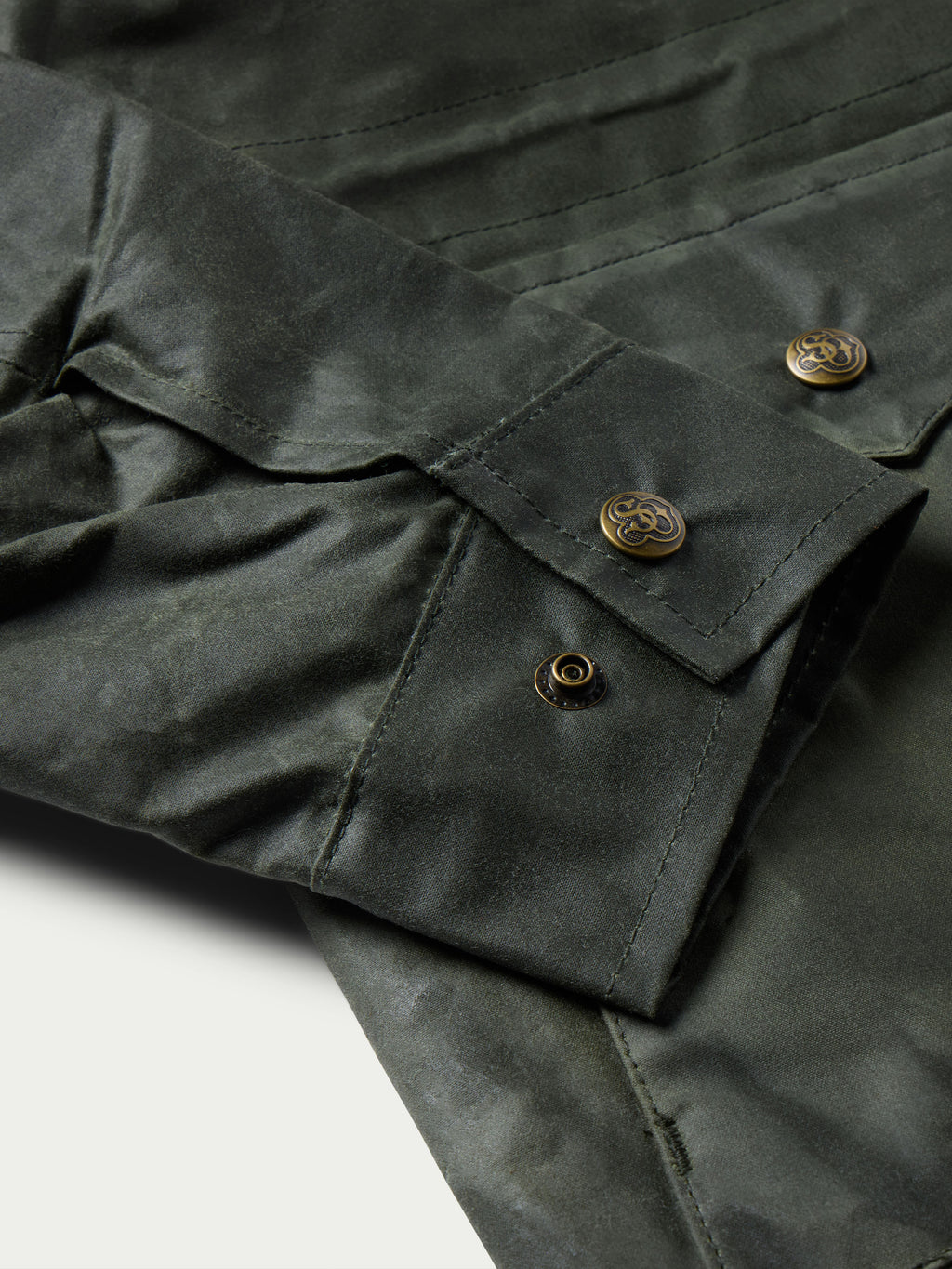 Dark green barn coat sleeve and pocket detail with gold-toned snap buttons and topstitching.