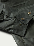 Dark green barn coat sleeve and pocket detail with gold-toned snap buttons and topstitching.