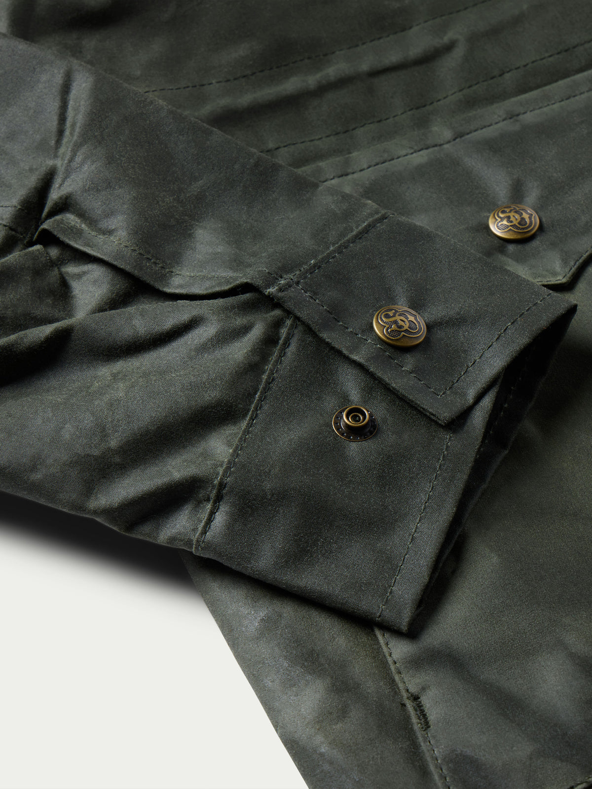 Dark green barn coat sleeve and pocket detail with gold-toned snap buttons and topstitching.