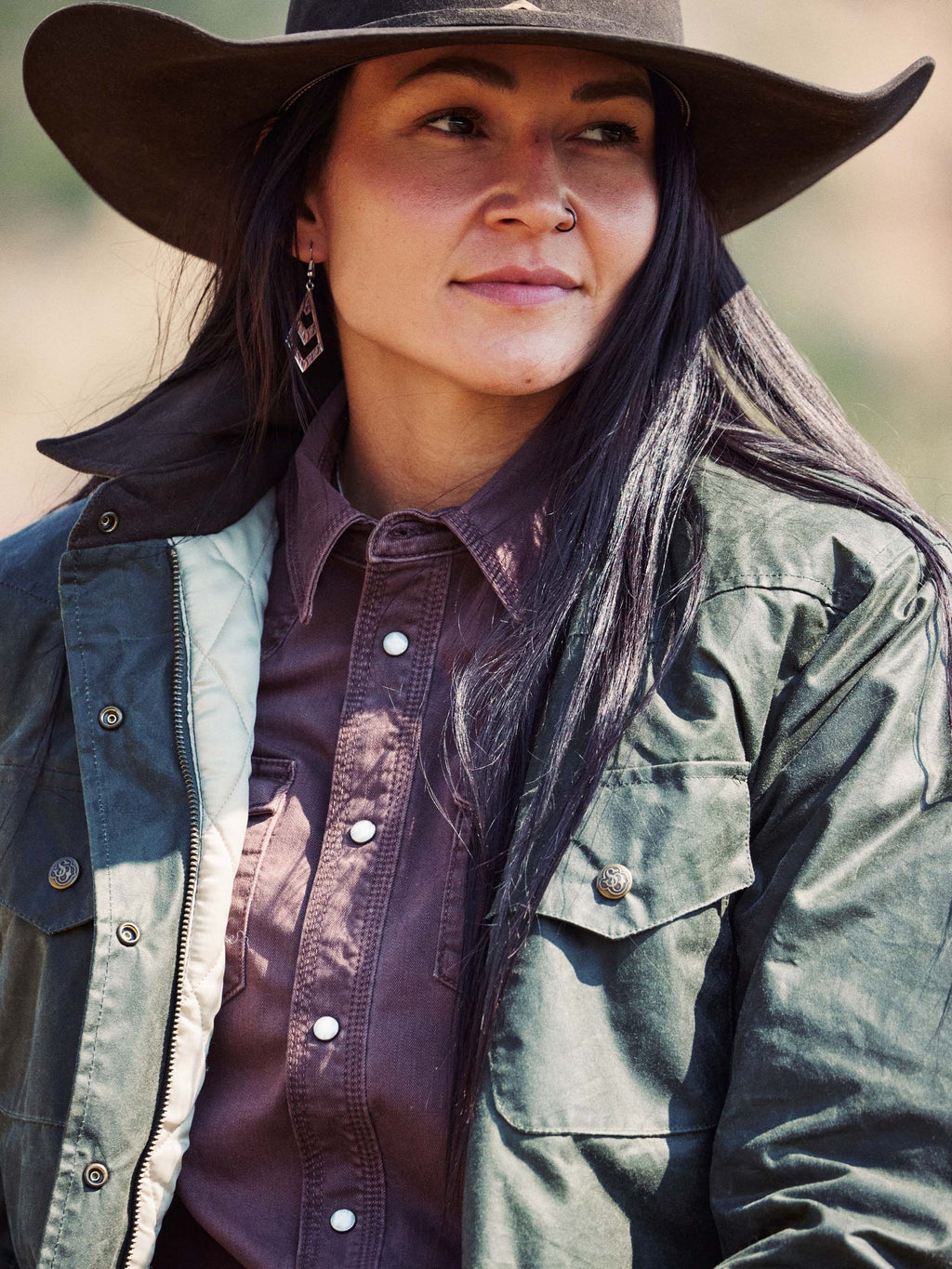 Model wearing dark green waxed barn coat with brown collar, snap pockets, and gold-toned buttons.