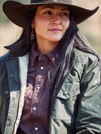 Model wearing dark green waxed barn coat with brown collar, snap pockets, and gold-toned buttons.