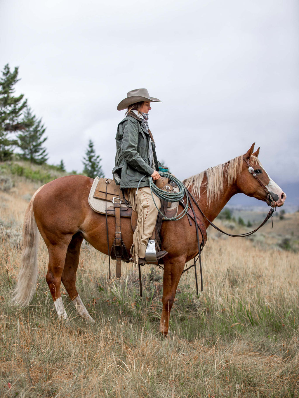Model wearing dark green waxed barn coat with brown collar and front pockets, riding outfit.