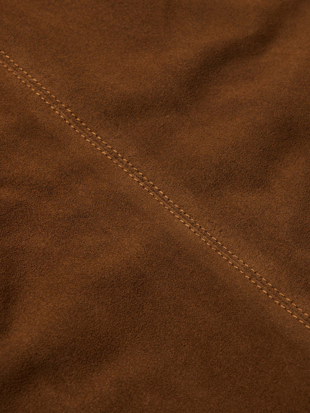 Close-up of pecan brown suede jacket with stitched seam detail along shoulder.
