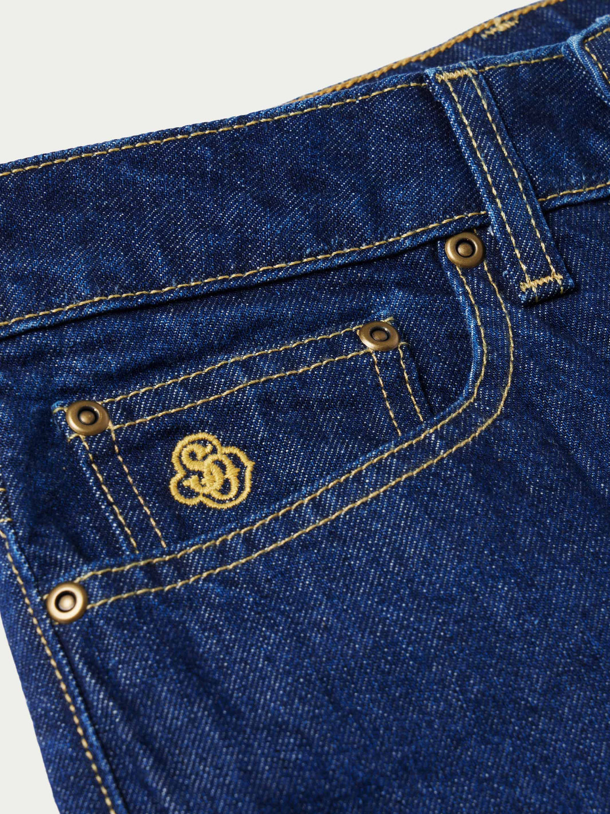 Dark indigo denim jeans close-up of button closure and pocket stitching