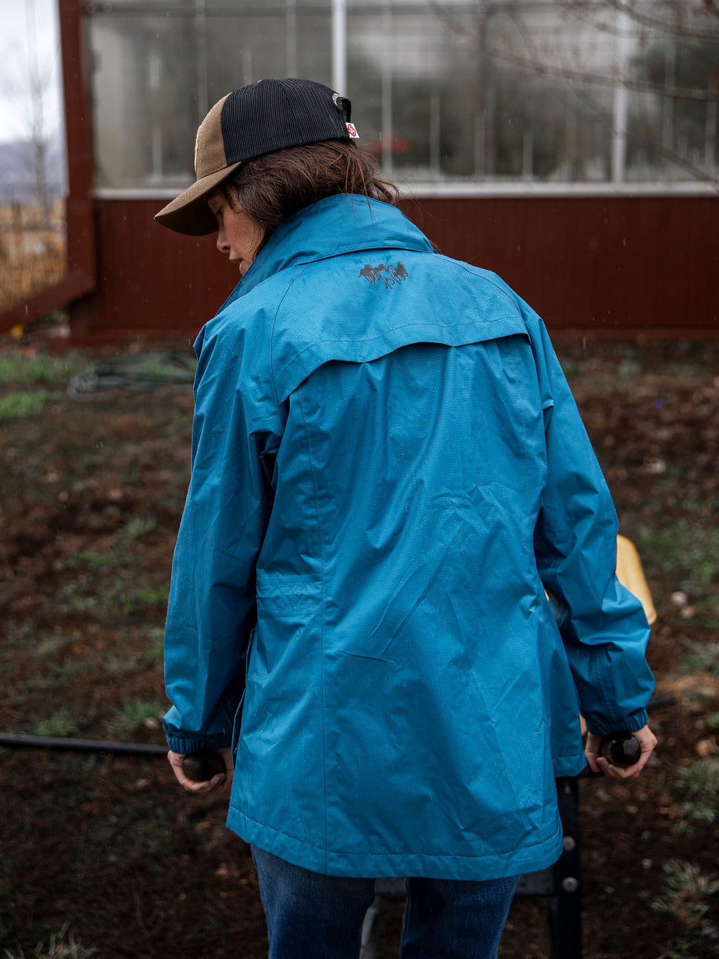 Blue hooded rain jacket with adjustable hem, back view