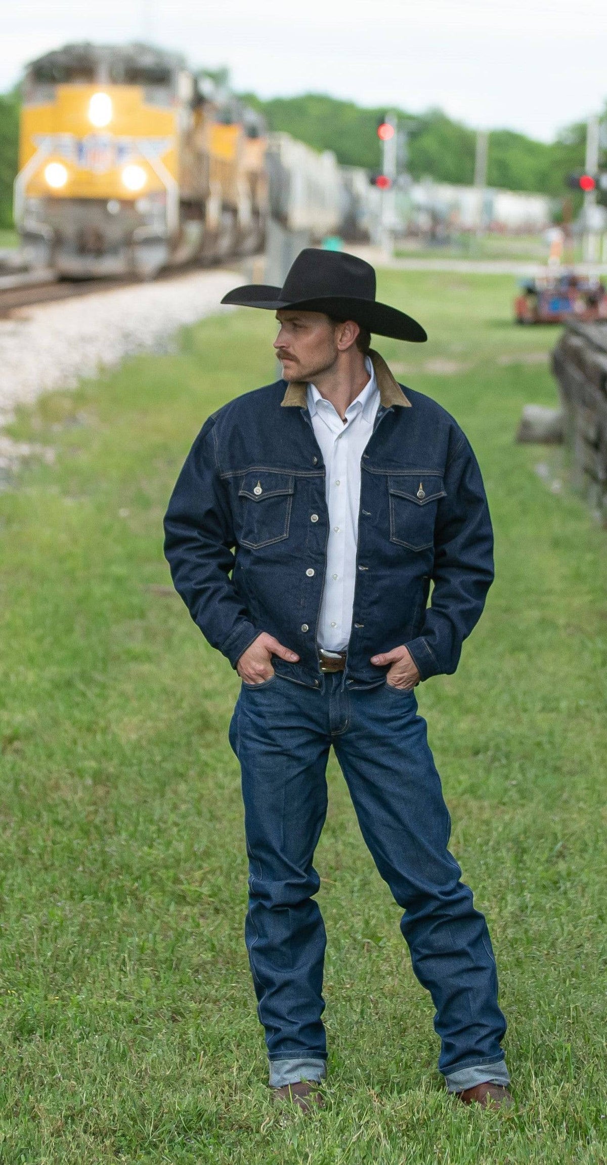 Blue denim dungarees on a man with belt and boots, standing outdoors.