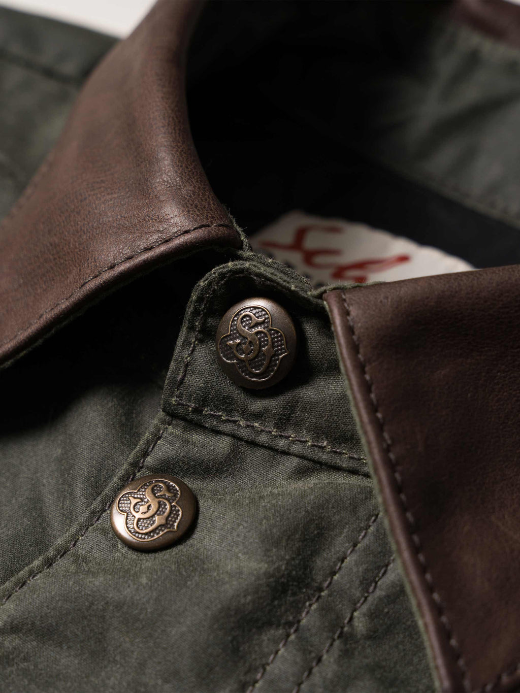 Dark green jacket close-up: brown leather-style collar and engraved snap buttons